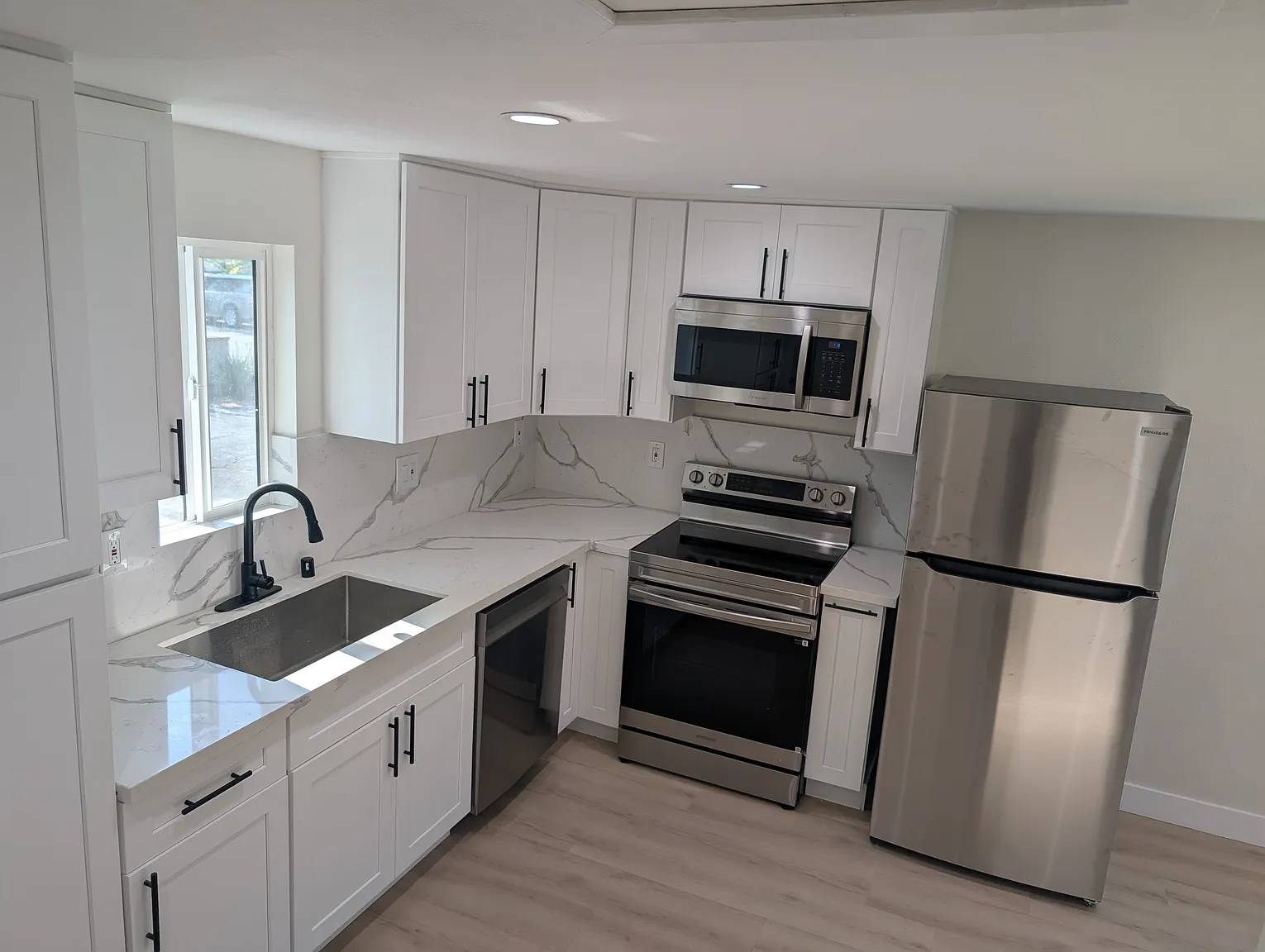 ADU kitchen with white shaker cabinets, quartz marble countertops, stainless steel appliances, and modern black hardware