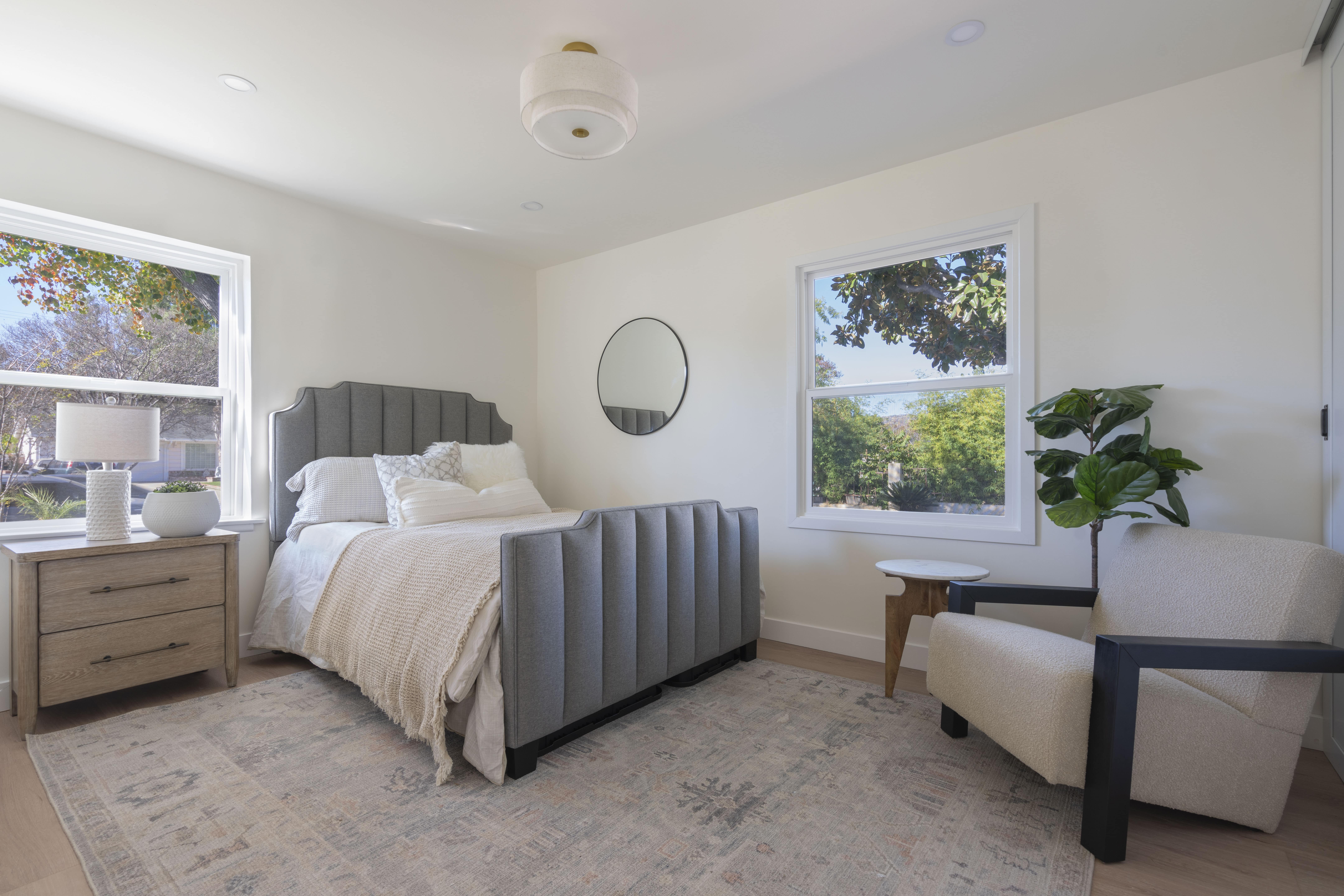 Elegant ADU primary bedroom with upholstered gray bed, natural light windows, and modern decor