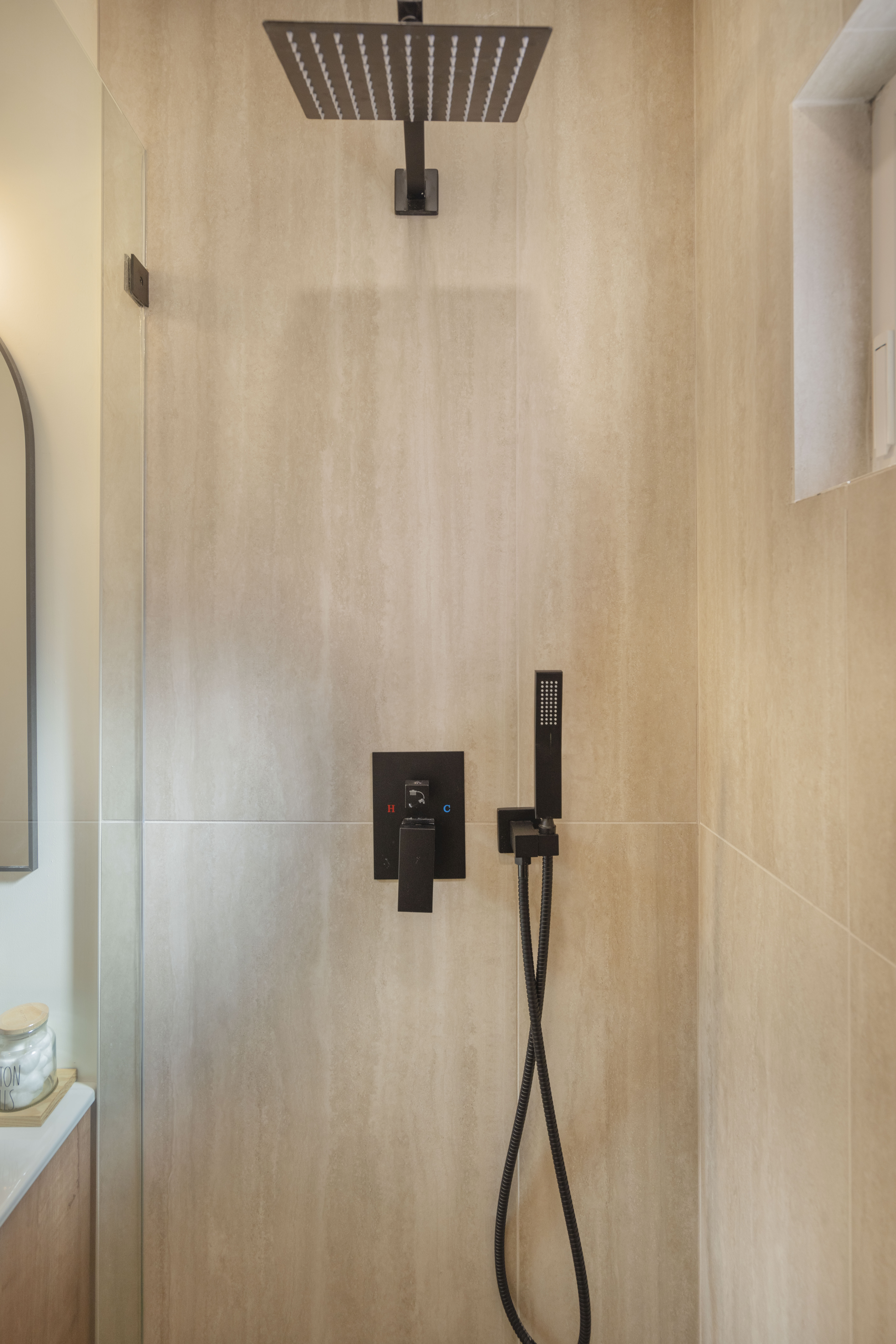 Luxury ADU rain shower with black fixtures, natural stone tile, and glass enclosure